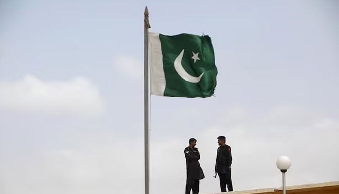 A Pakistani flag flies on a mast as paramilitary Frontier Corps soldiers talk while guarding at Karachis District Malir prison, August 23, 2013. — Reuters
