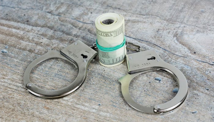 Representational image showing handcuffs and cash symbolising corruption or financial crime. — Unsplash/file