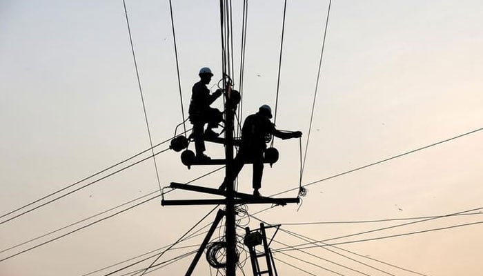 Technicians are silhouetted as they fix cables on a power transmission line in Karachi. — Reuters/File