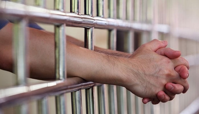 A prisoner clasps his hands behind jail bars in this undated image. — AFP