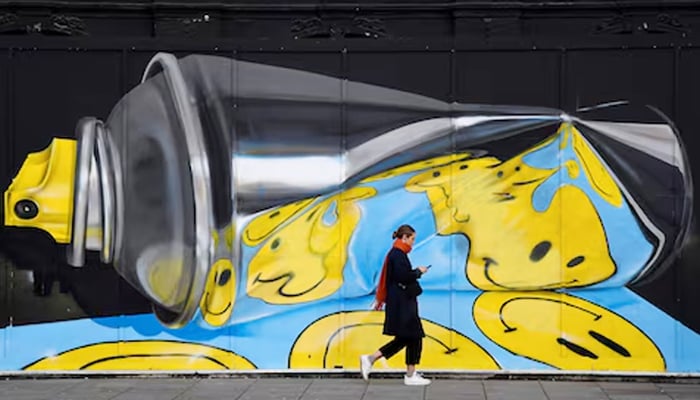A woman views her phone as she walks past street art on a wall in London, Britain, December 18, 2019. — Reuters