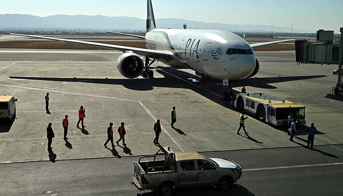 Ground staff stand next to the Pakistan International Airlines (PIA) aircraft ahead of its takeoff for Paris at the Islamabad International Airport on January 10, 2025. — INP