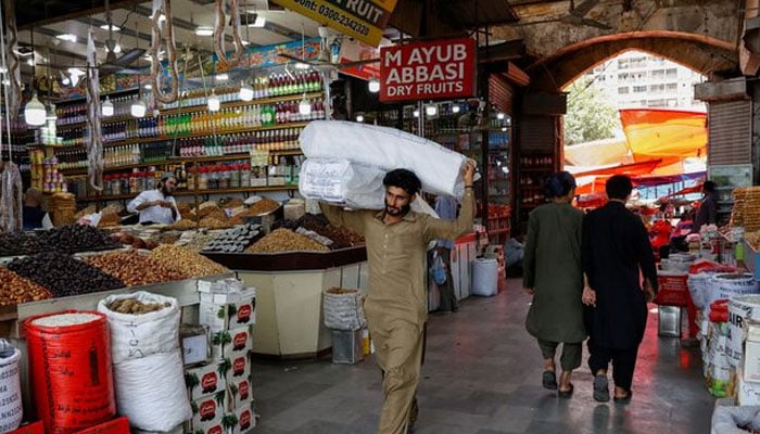 A man walks with sacks of supplies on his shoulder to deliver to a nearby shop at a market in Karachi, on June 11, 2024. — Reuters