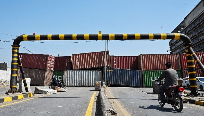 A motorcyclist rides past a closed street as containers are placed in front of the road leading to the US Consulate in Karachi on March 2, 2026. — AFP