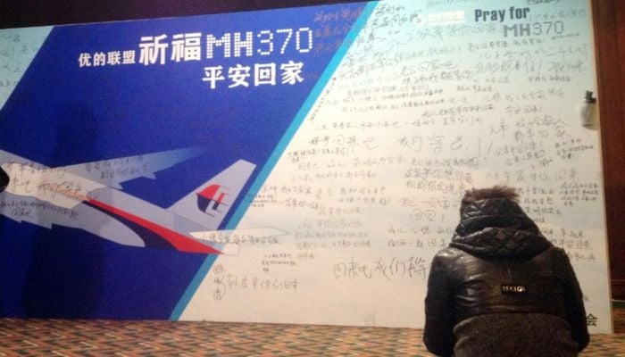 A woman sits before a board filled with prayers and messages written by relatives to the missing passengers of Malaysia Airlines flight MH370. — AFP