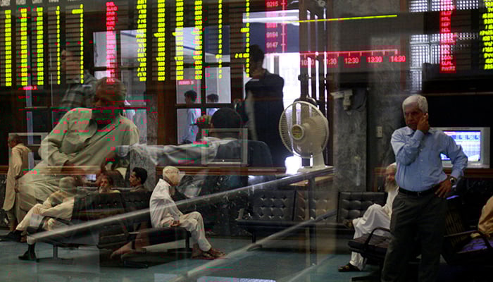 Stockbrokers are seen near an electronic display board during a trading session at the Stock Exchange in Karachi. — Reuters