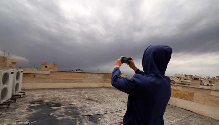 A resident takes pictures while standing on the roof of his house covered with soot after overnight strike on the Tehran Oil Refinery in Tehran on March 8, 2026. — AFP