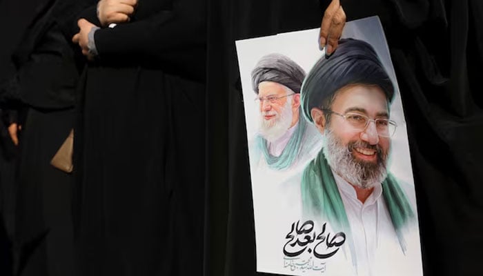 A woman holds an image of Irans new supreme leader, Mojtaba Khamenei, alongside late Iranian Supreme Leader Ayatollah Ali Khamenei, during a funeral ceremony for the Iranian military commanders who were killed in strikes, amid the US-Israeli conflict with Iran, in Tehran, Iran, March 11, 2026. — Reuters
