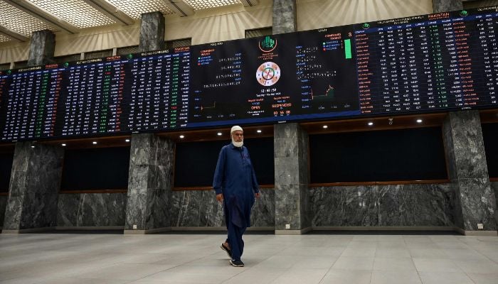 A stock broker walks past a digital board showing share prices at the Pakistan Stock Exchange (PSX) in Karachi on March 10, 2026. — AFP