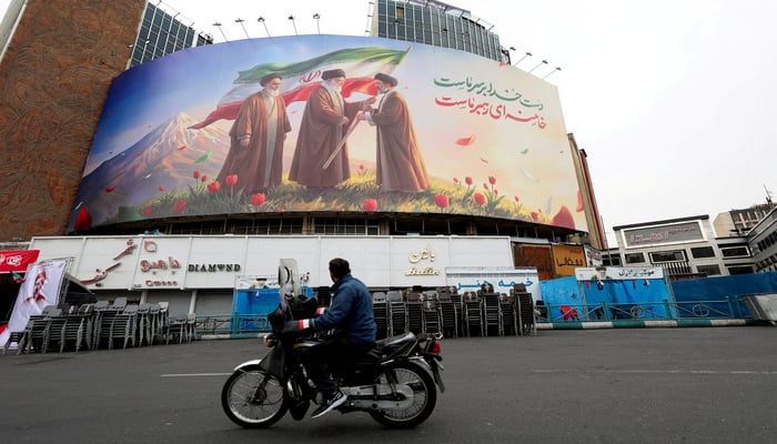 A man on a motorcycle looks at a large billboard featuring Irans new Supreme Leader Mojtaba Khamenei, and late Supreme Leaders Ayatollah Ali Khamenei and Ayatollah Ruhollah Khomeini, amid the US-Israeli conflict with Iran, in Tehran, Iran, March 12, 2026. — Reuters