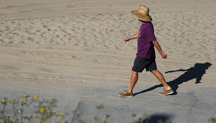 A person wears a hat for shade under the morning sun while walking along The Strand in Redondo Beach, California on March 20, 2026, during a heat wave. — AFP