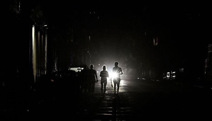 People walk on a street without electricity during a nation wide blackout in Havana on March 21, 2026. — AFP