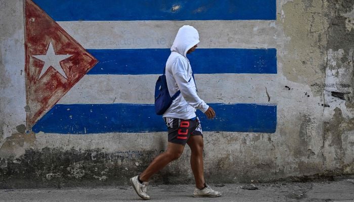 A man walks past a wall painted with a Cuban flag on a street in Havana during a nationwide blackout on March 22, 2026. — AFP