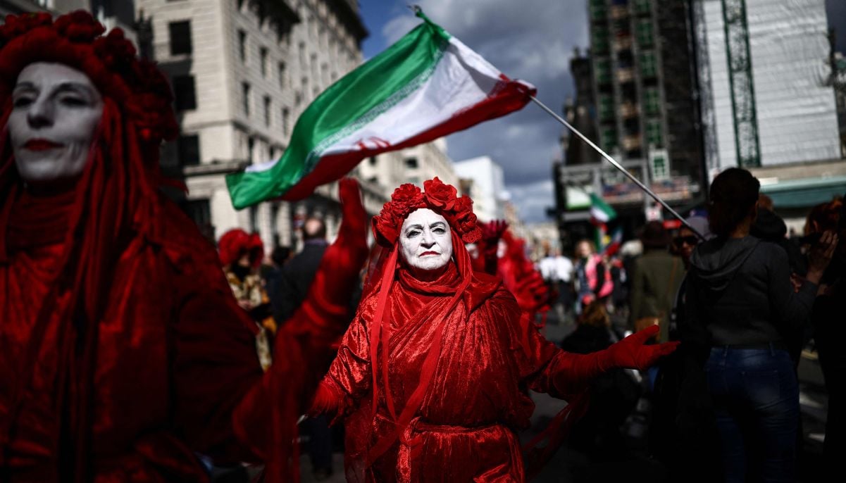 Members of the ´Red Rebel Brigade´, a climate activist group, walk past Iranian flags being displayed as they join a march against the far right, organised by the Together Alliance, in central London on March 28, 2026. — AFP