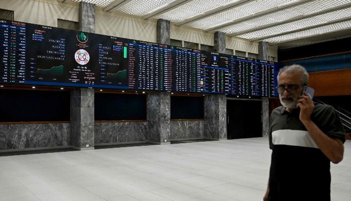 A stockbroker walks past a digital board showing share prices at the Pakistan Stock Exchange (PSX) in Karachi on March 25, 2026. — AFP