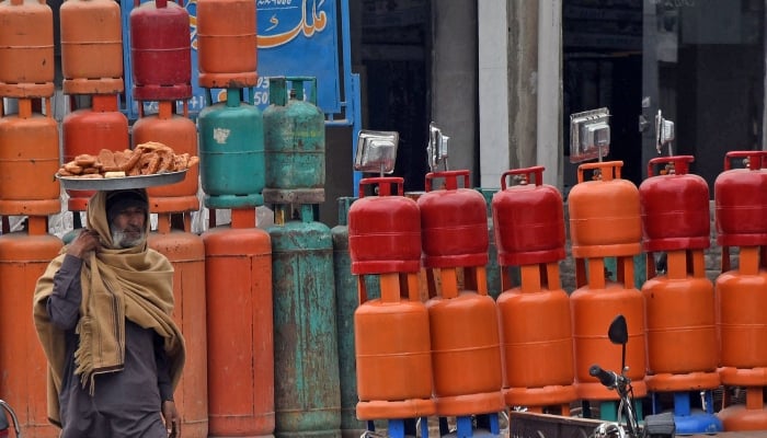 A street vendor carrying traditional food items on his head walk past in front of LPG gas cylinders at sector G-11 road in Islamabad. — Online/File