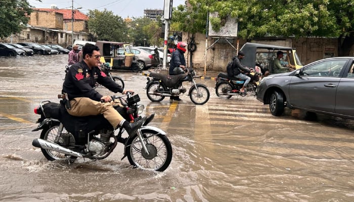 A policeman tries to evade water while riding his bike through flooded road after heavy rainfall in Karachi on April 2, 2026. — Geo.tv
