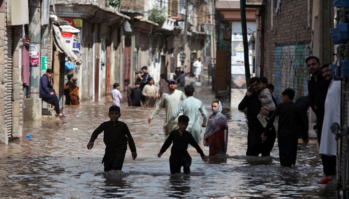 People wade through a water-logged street following heavy rains in Peshawar, April 4, 2026. — Reuters