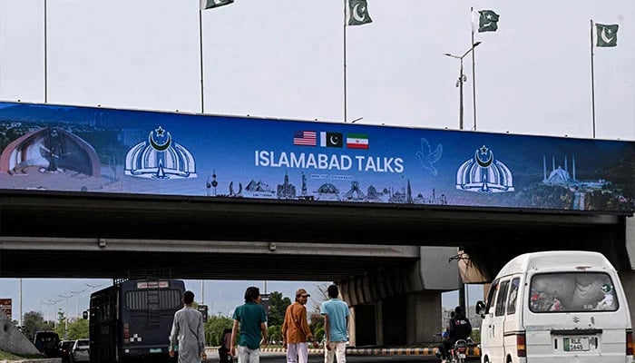 Boys walk under a digital screen displaying news of US-Iran peace talks along a road in Islamabad on April 10, 2026. — AFP