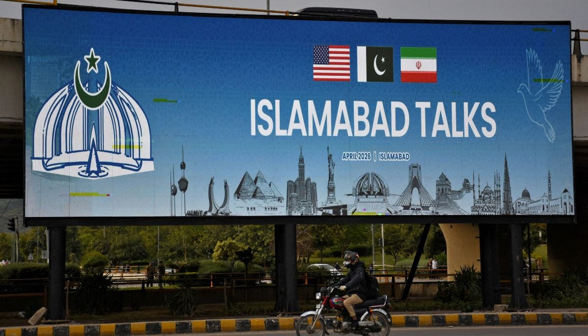 A man rides his motorbike past a billboard installed alongside a road as as delegations from the United States and Iran are expected to hold peace talks in Islamabad, April 11, 2026. — Reuters
