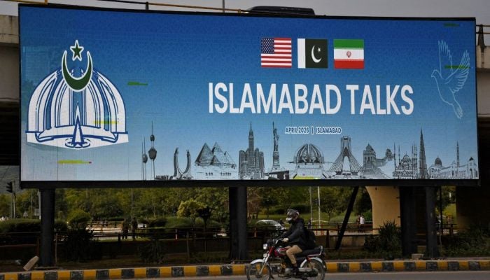 A man rides his motorbike past a billboard installed alongside a road as as delegations from the United States and Iran are expected to hold peace talks in Islamabad, April 11, 2026. — Reuters