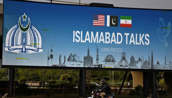 A man rides his motorbike past a billboard installed alongside a road as as delegations from the United States and Iran are expected to hold peace talks in Islamabad, April 11, 2026. — Reuters