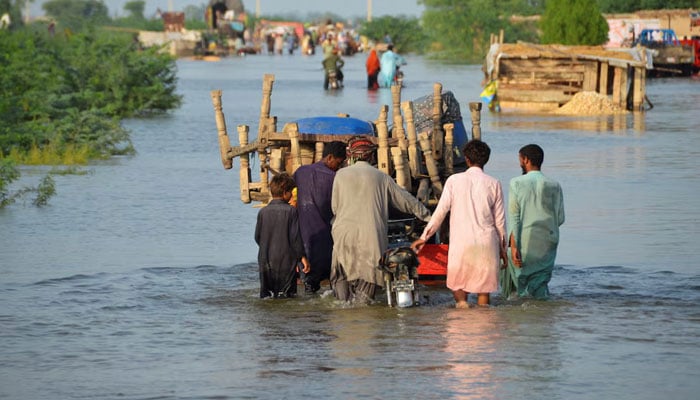 Men walk along a flooded road with their belongings, following rains and floods during the monsoon season in Sohbatpur, August 28, 2022. — Reuters