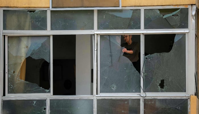 A displaced woman removes shattered glass from the windows of her damaged property in Beirut, Lebanon on April 18, 2026. — AFP