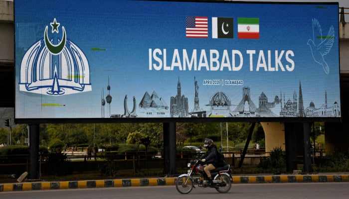 A man rides his motorbike past a billboard installed alongside a road as Pakistan prepares to host the U.S. and Iran for peace talks, in Islamabad, Pakistan, April 10, 2026. — Reuters