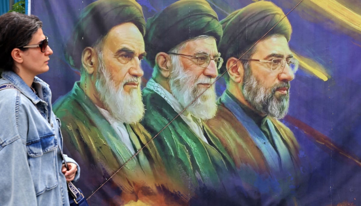A woman walks past a banner featuring Iran´s late supreme leaders Ayatollah Ruhollah Khomeini (left) and Ayatollah Ali Khamenei (centre) next to newly elected supreme leader Ayatollah Mojtaba Khamenei, in Tehran on April 19, 2026. — AFP