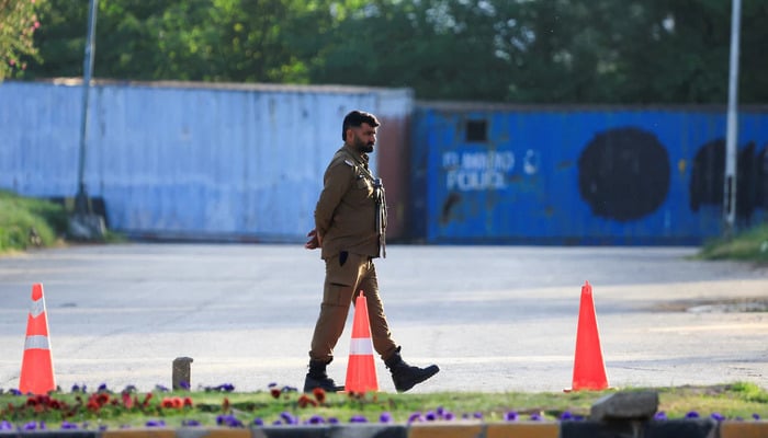 A police officer guards a road blocked with shipping containers, for security measures at D Chowk near the Presidents House as Pakistan prepares to host the United States and Iran for the second phase of peace talks in Islamabad, April 20, 2026. — Reuters