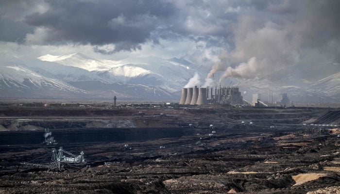 Mining vehicles extract coal from a lignite coal mine, as the Elbistan thermal power plant, is seen in the background in Elbistan on February 11, 2026. — AFP