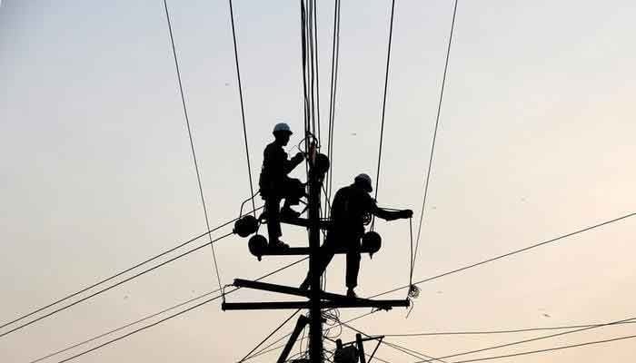 Technicians are silhouetted as they fix cables on a power transmission line in Karachi, January 9, 2017. — Reuters