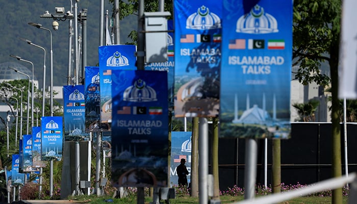 A silhouetted man stands next to advertisement posters reading “Islamabad Talks” at the Convention Centre in Islamabad, April 22, 2026. — Reuters