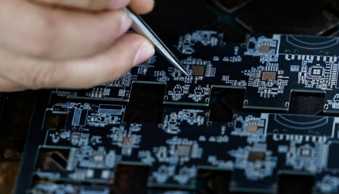 An employee uses a pair of tweezers to adjust microchips and electronic components on a printed circuit board at a factory, which is in partnership with Agilian Technology, in Dongguan, Guangdong province, China, March 16, 2026. — Reuters
