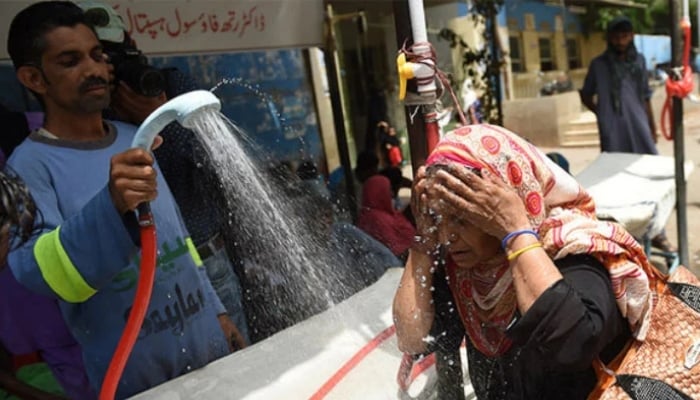 A volunteer showers a woman with water during a heatwave in Karachi. — AFP/File