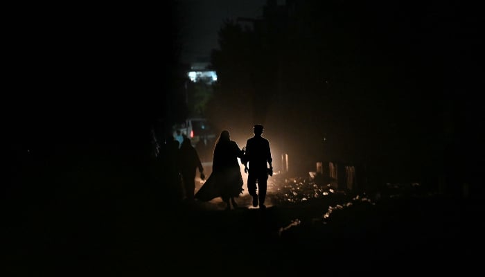 Commuters walk along a street during a power cut in Karachi on April 19, 2026. — AFP