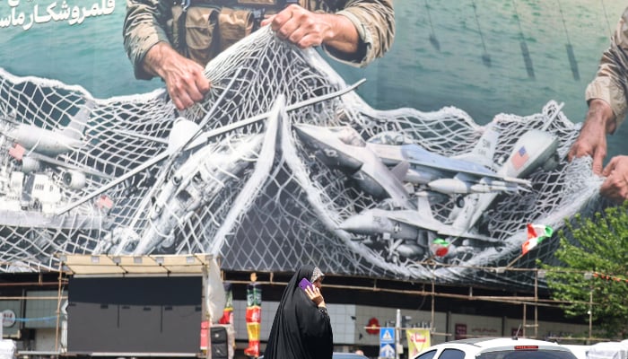 A woman walks past a giant billboard reading The Strait of Hormuz remains closed at the Revolution Square in Tehran on April 28, 2026. — AFP