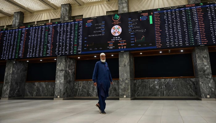 A stockbroker walks past a digital board showing share prices at the Pakistan Stock Exchange (PSX) in Karachi on March 10, 2026. — AFP