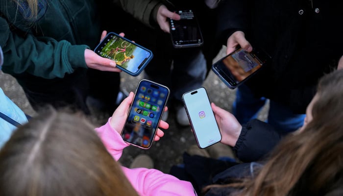Teenagers pose for a picture while looking at their phones, in Bonn, Germany, February 20, 2026. — Reuters
