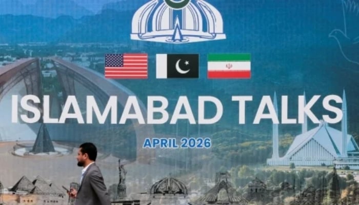 A man walks past a billboard near the media centre as delegations from the United States and Iran are expected to hold peace talks in Islamabad, on April 11, 2026. — Reuters