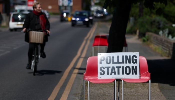 A person cycles near a sign placed on chairs outside a polling station during local elections in Jaywick, near Clacton-on-Sea, Britain, May 7, 2026. — Reuters