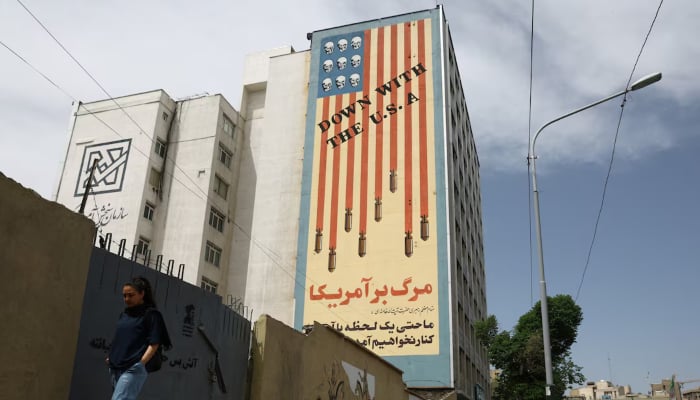 A woman walks past an anti-US mural on a building in Tehran, Iran, May 8, 2026. — Reuters
