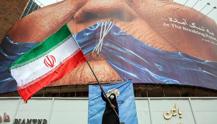 A woman waves an Iranian flag in front of an anti-US billboard referring to US President Donald Trump and the Strait of Hormuz at Valiasr Square in Tehran on May 5, 2026. — AFP
