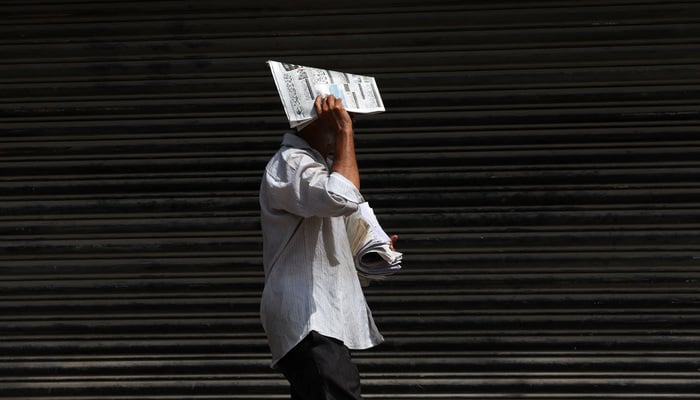 A newspaper hawker walks while covering his face with a newspaper to avoid sunlight, during a hot summer day in Karachi on May 5, 2026. — Reuters