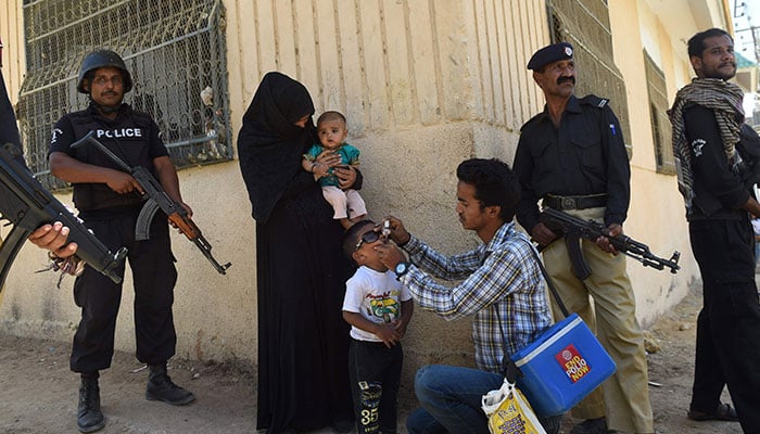 This representational image shows policemen stand guard as a health worker administers polio drops to a child during a polio vaccination campaign in Karachi. ─ AFP/File