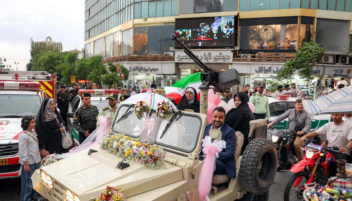 A bride and group couple rides in a military jeep arriving for a public mass wedding ceremony at Imam Hossein Square in Tehran on May 18, 2026. — AFP