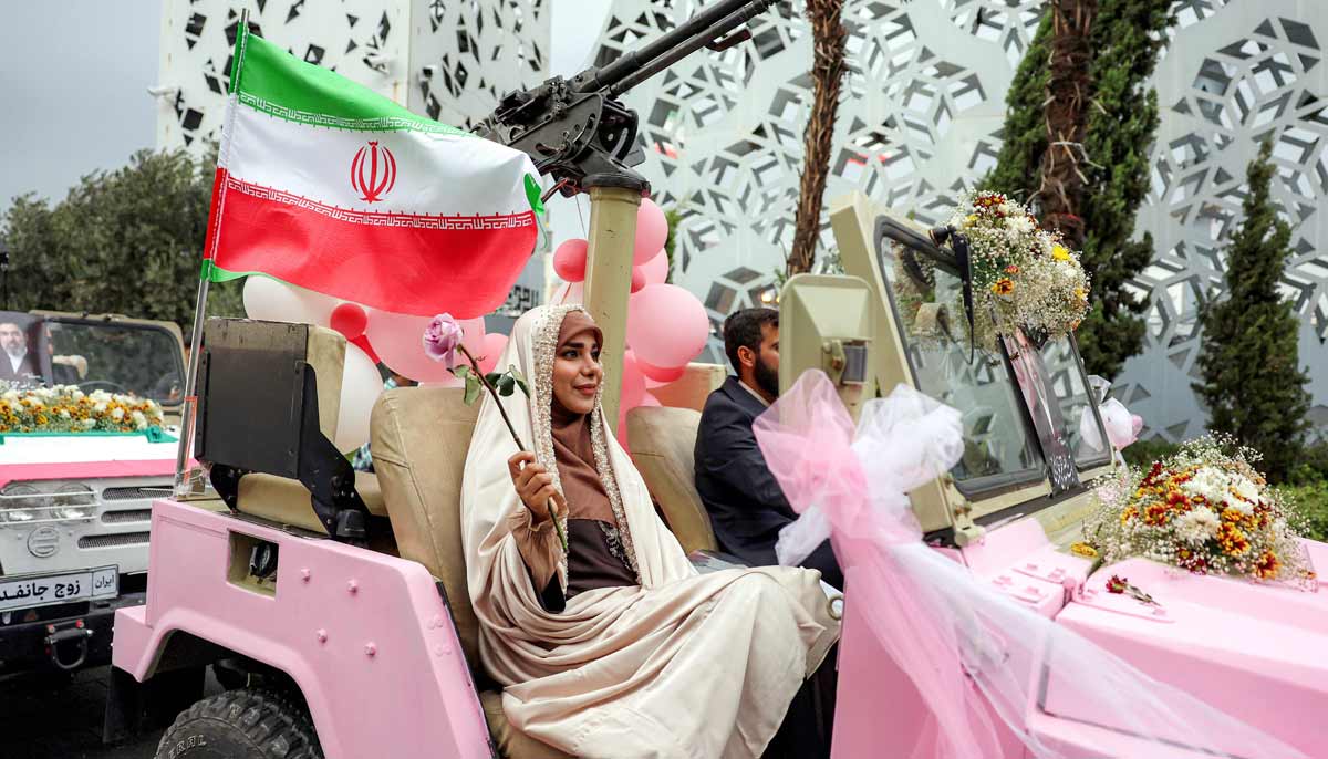 A bride and group couple rides in a military jeep arriving for a public mass wedding ceremony at Imam Hossein Square in Tehran on May 18, 2026. — AFP