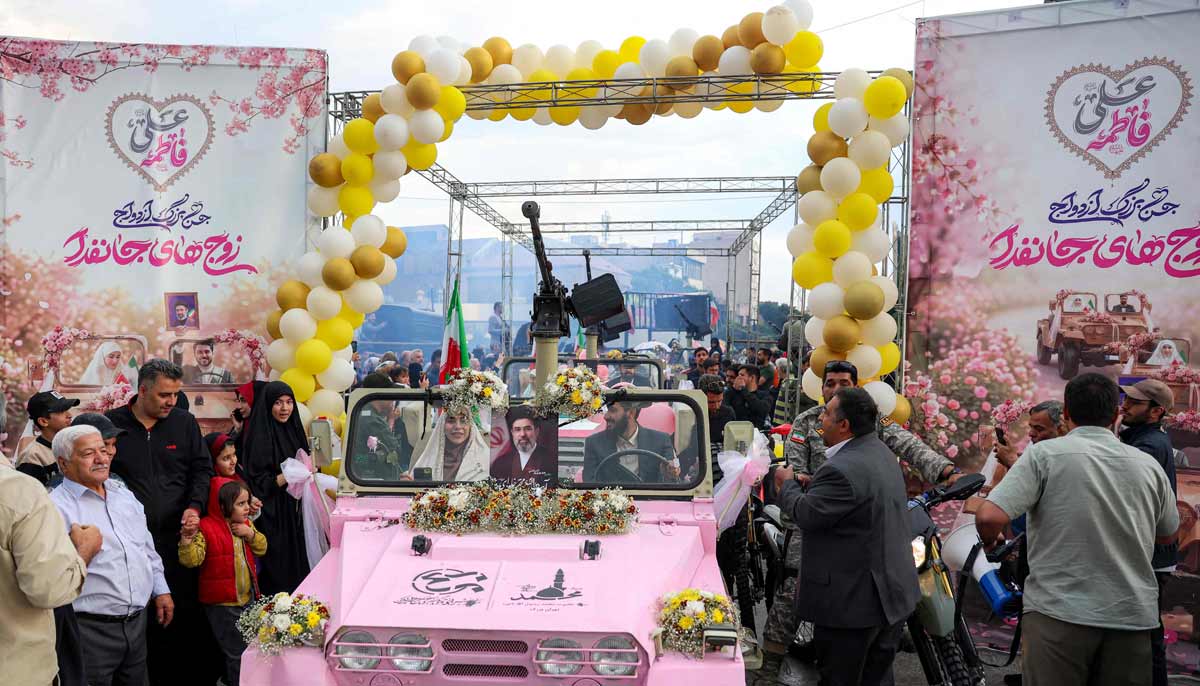 A bride and group couple rides in a military jeep arriving for a public mass wedding ceremony at Imam Hossein Square in Tehran on May 18, 2026.— AFP