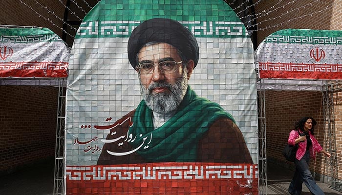 A woman walks next to a banner with a picture of Irans new Supreme Leader Mojtaba Khamenei in Tehran, Iran, May 8, 2026. — Reuters
